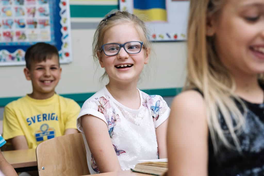 Kinderergotherapie in de klas meisje met bril lacht naar camera