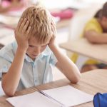 Jongen steunt met hoofd op handen boven schoolwerk